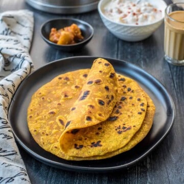 A black plate with a small stack of masala roti with the top one curled up a little.