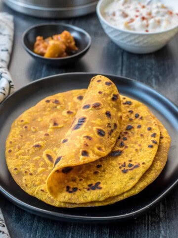 A black plate with a small stack of masala roti with the top one curled up a little.
