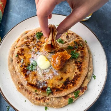 A hand taking a portion of cheese paratha.