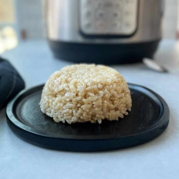 A form of brown rice on a black plate, with an Instant Pot in the background.