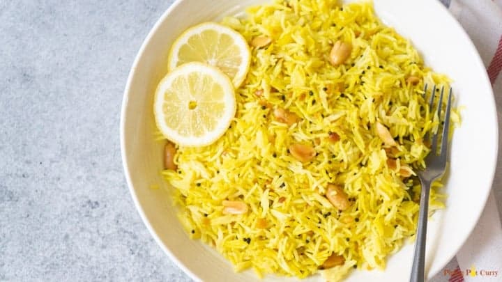 Lemon rice served in a white bowl topped with lemon slices