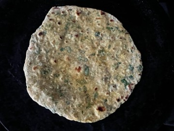 A paratha cooking in a tawa with browned spots.
