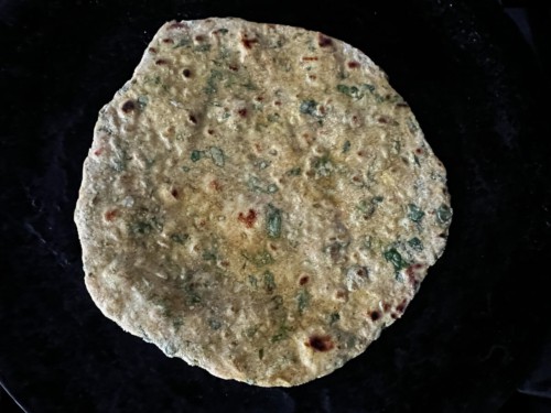 A paratha cooking in a tawa with browned spots.