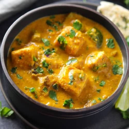 Paneer tikka masala served in a black bowl with lime slices and naan