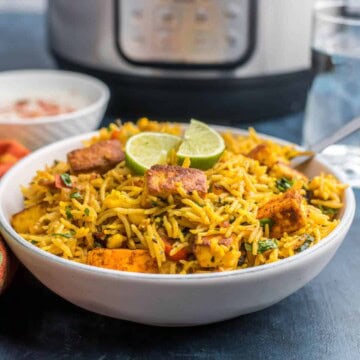 White bowl with paneer biryani, topped with two slices of lime.