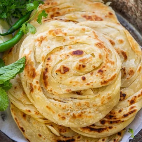 Kerala parotta stacked on a pewter plate with green chilies, mint leaves and lime slices