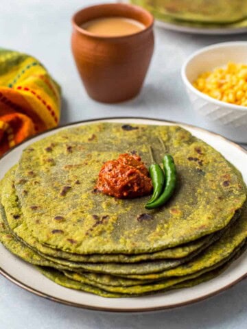Stack of palak parathas on a white plate with dollop of chili sauce on top.
