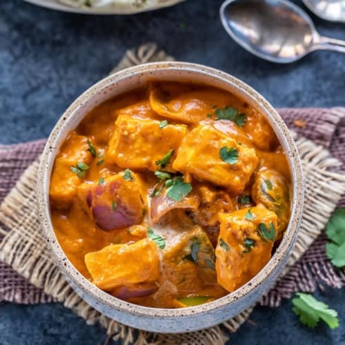 Paneer tikka masala served in a bowl kept over a blue table