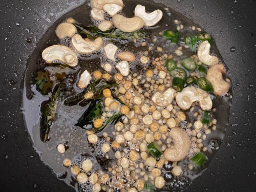 Curry leaves, cashews, chana dal, urad dal added to oil in a black non-stick wok