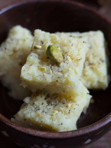 4 pieces of coconut barfi stacked in a brown bowl