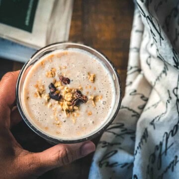 An overhead shot of a hand holding a glass of apple banana smoothie