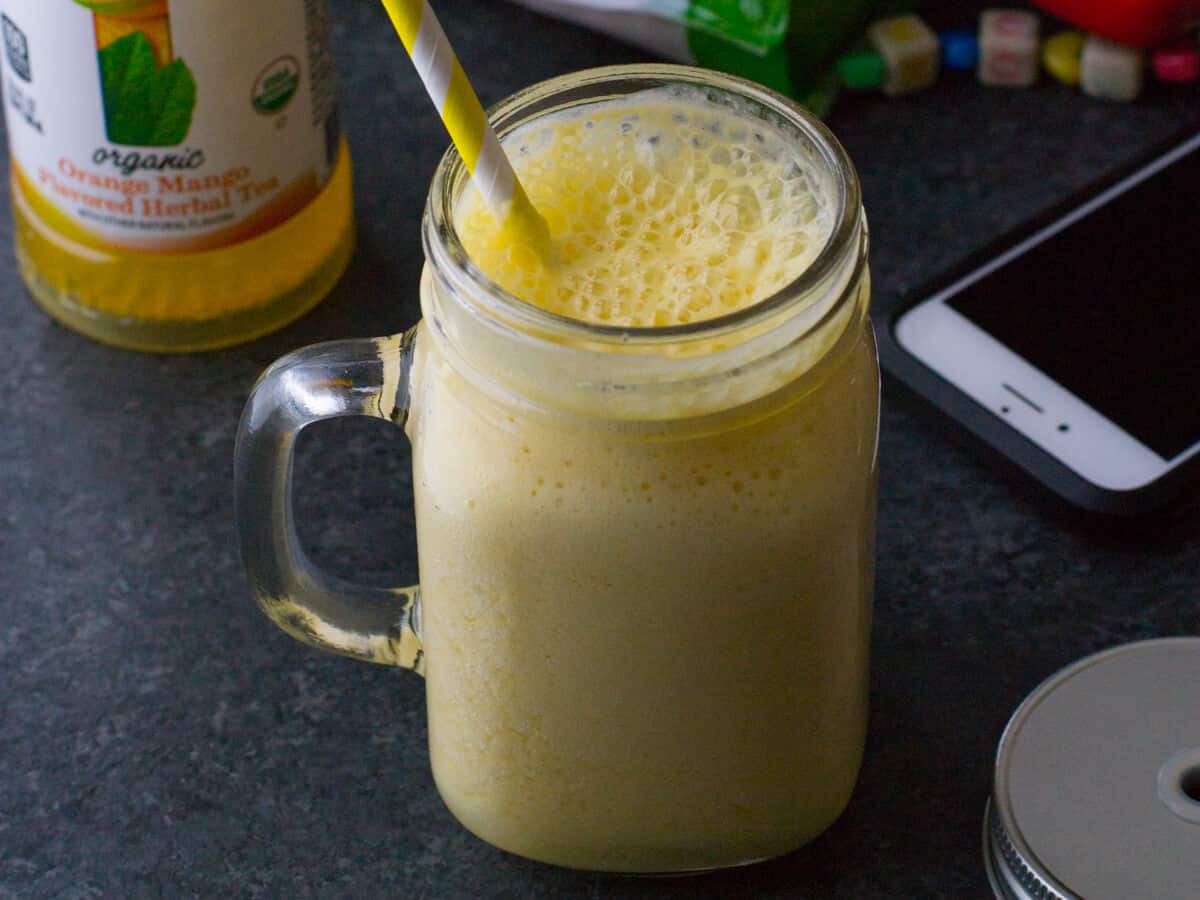Pineapple orange smoothie served in a ball jar with a phone on the side