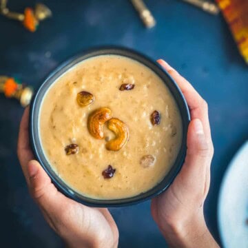 A hand holding a bowl of moong dal payasam served in a black bowl