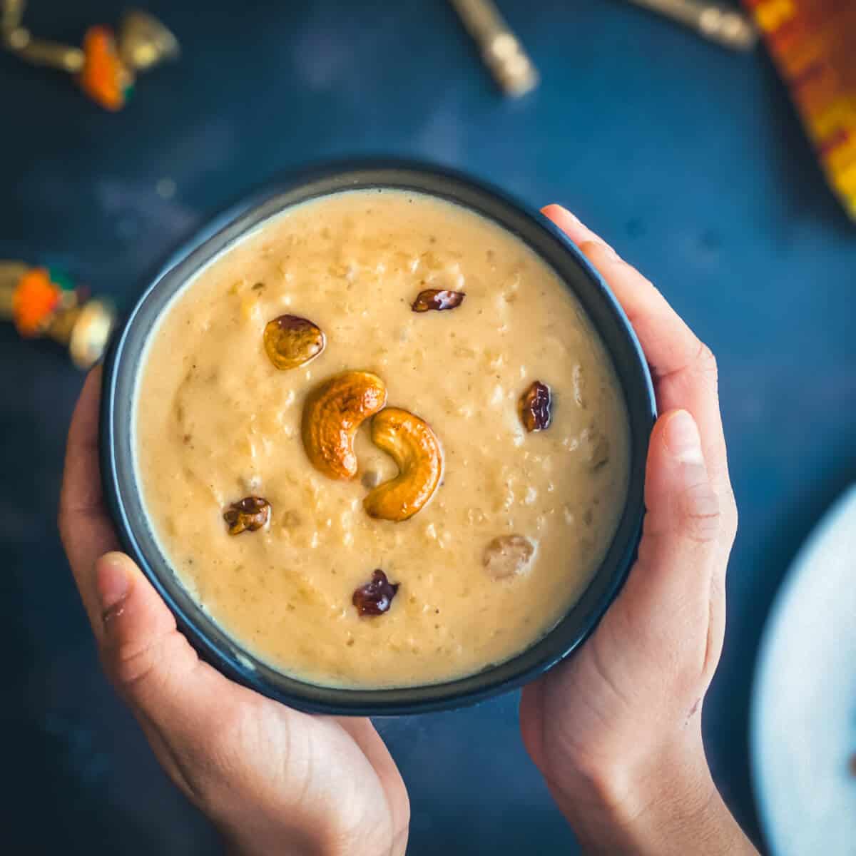 A hand holding a bowl of moong dal payasam served in a black bowl