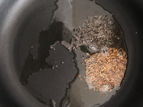 Mustard seeds and cumin seeds added to ghee in a pan
