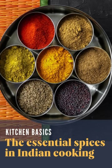 A masala dabba (spice tin) with 7 spices placed on an orange mat with caption " The essential spices in Indian cooking"