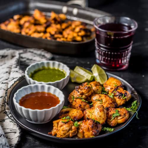 Chicken tikka served with green chutney and tamarind chutney along with lemon wedges with a glass of grape juice on the side