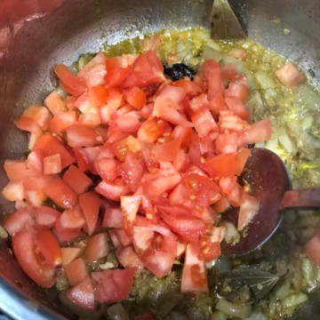 Tomatoes added to an onion base in a steel pot
