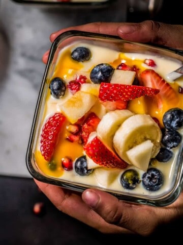 An overhead shot of a child holding a bowl of fruit custard. Another bowl is placed on a marble board.